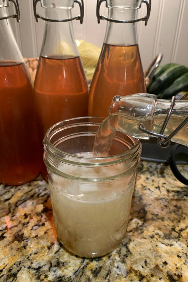 glass bottle pouring water kefir in a glass filled with ice